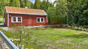A red wooden house with a metal roof, surrounded by a grassy field and dense forest. - Nice home in Hovsherad with WiFi (Hovsherad)