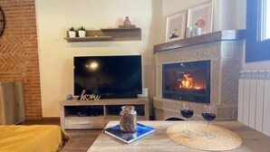 Un salon chaleureux avec une cheminée, un téléviseur à écran plat et une table basse sur laquelle reposent deux verres de vin.