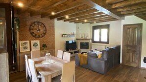 Un vaste espace de vie doté d’un plafond en bois, d’une table à manger avec des chaises, d’un canapé gris et d’un téléviseur.