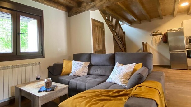 Un salon chaleureux avec un plafond en bois, un canapé gris agrémenté de coussins, une table basse et un plaid de couleur moutarde.