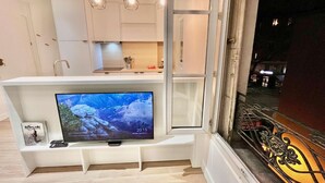 A modern living room with a flat-screen TV, white cabinetry, and a balcony with a railing. - Le Victor Hugo - Clichy-la-Garenne (Clichy)