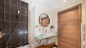 Une salle de bain moderne avec une baignoire, une douche à parois de verre, une porte en bois et un miroir au-dessus du lavabo.