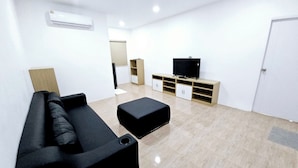 A modern living room with a black sofa, a black ottoman, a TV on a wooden stand, and a white door. - Suvarn Gleaw Thong Resort (Trat)