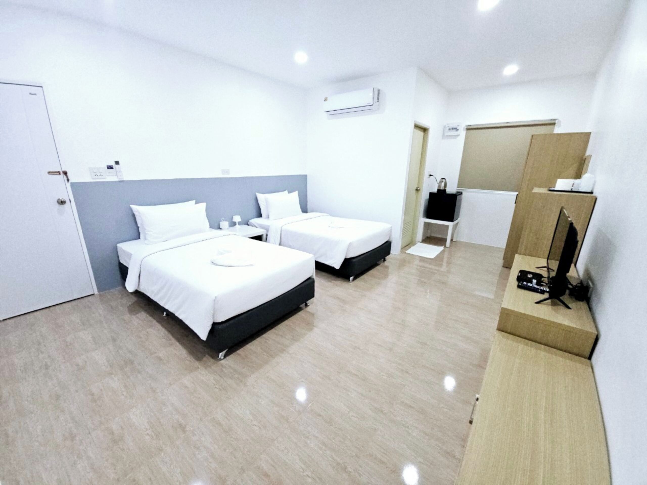 A hotel room with two beds, a desk, a TV on a stand, and an air conditioning unit.