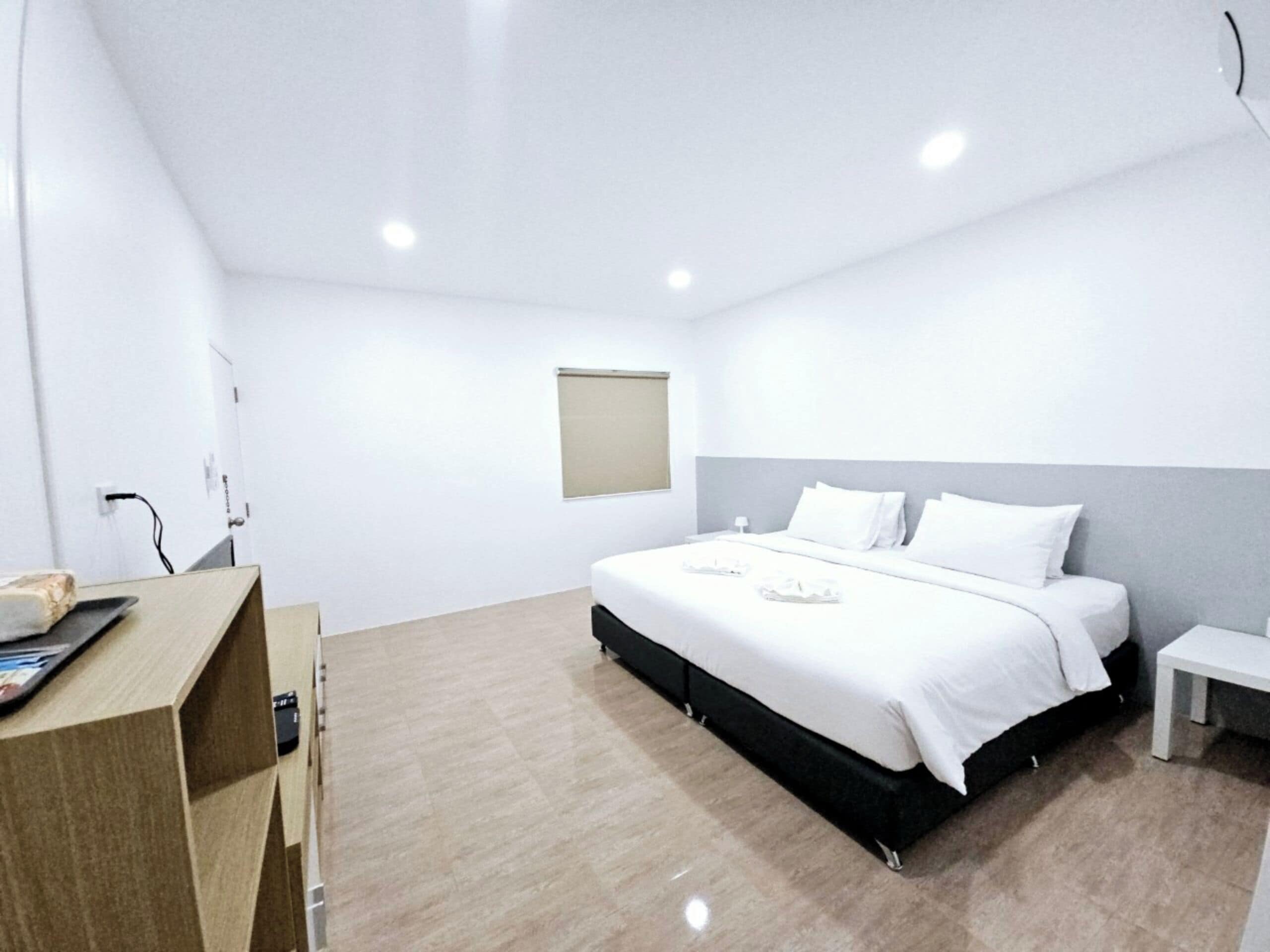 A modern hotel room with a large bed, bedside tables, a desk, and a small window.