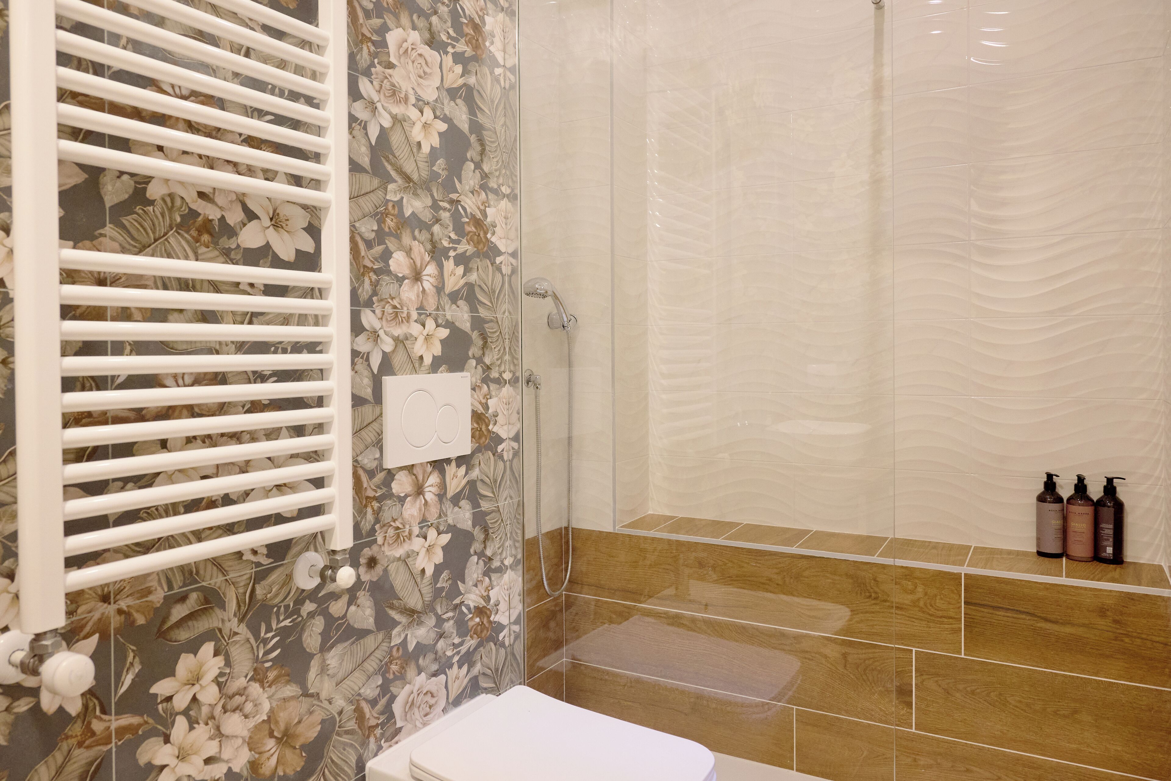 A bathroom with a shower, toilet, and a floral-patterned wall.