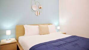 Ein ordentlich bezogenes Bett mit einer blauen Tagesdecke, einem hölzernen Kopfteil und zwei Nachttischlampen.