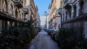 Eine schmale Stadtstraße, gesäumt von parkenden Autos und Gebäuden mit aufwendigen Fassaden.