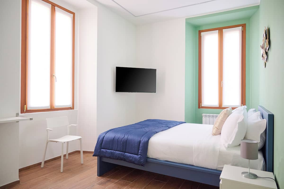 Ein Schlafzimmer mit Bett, Sessel, Fernseher und Fenster.