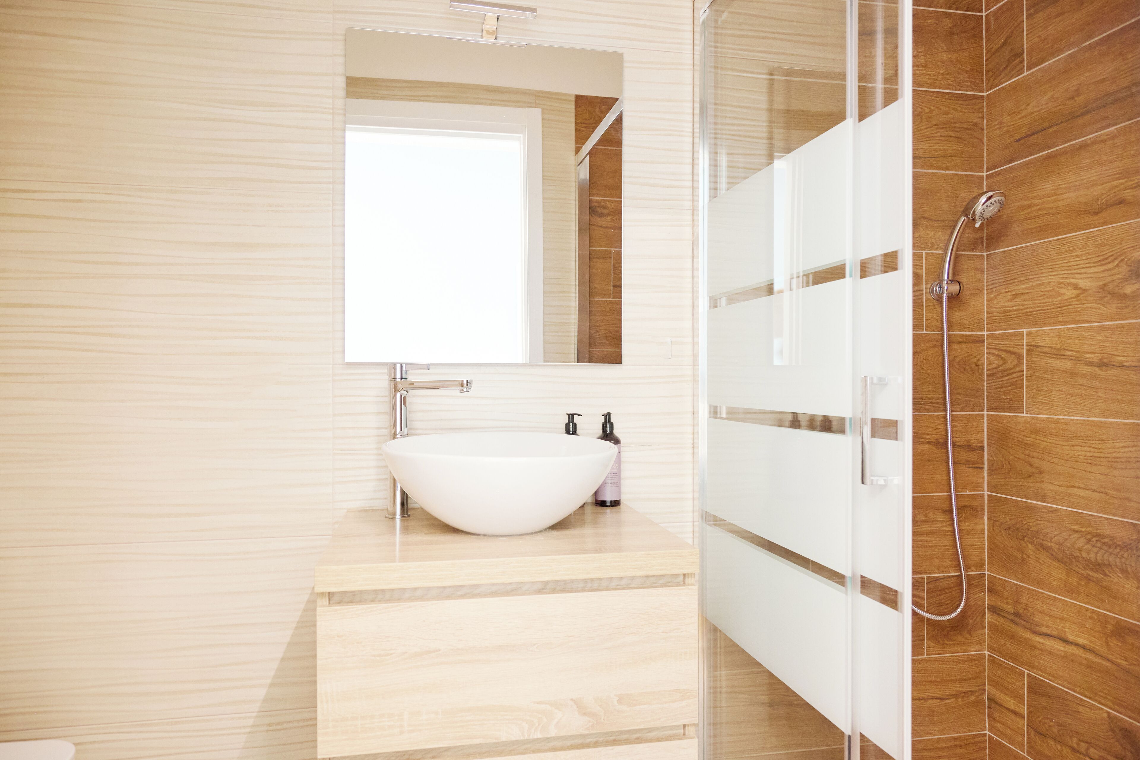Une salle de bain moderne avec un grand lavabo blanc, un miroir au-dessus et un espace douche aux carreaux en bois.