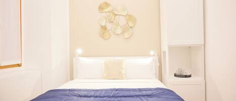 A neatly made bed with a blue blanket, white pillows, and a decorative wall piece above it.