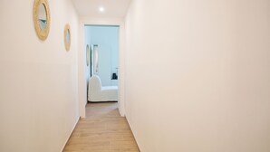 Ein schmaler Korridor mit Holzboden und weißen Wänden. Im Hintergrund sind zwei runde Wandverzierungen und ein weißer Stuhl zu sehen.