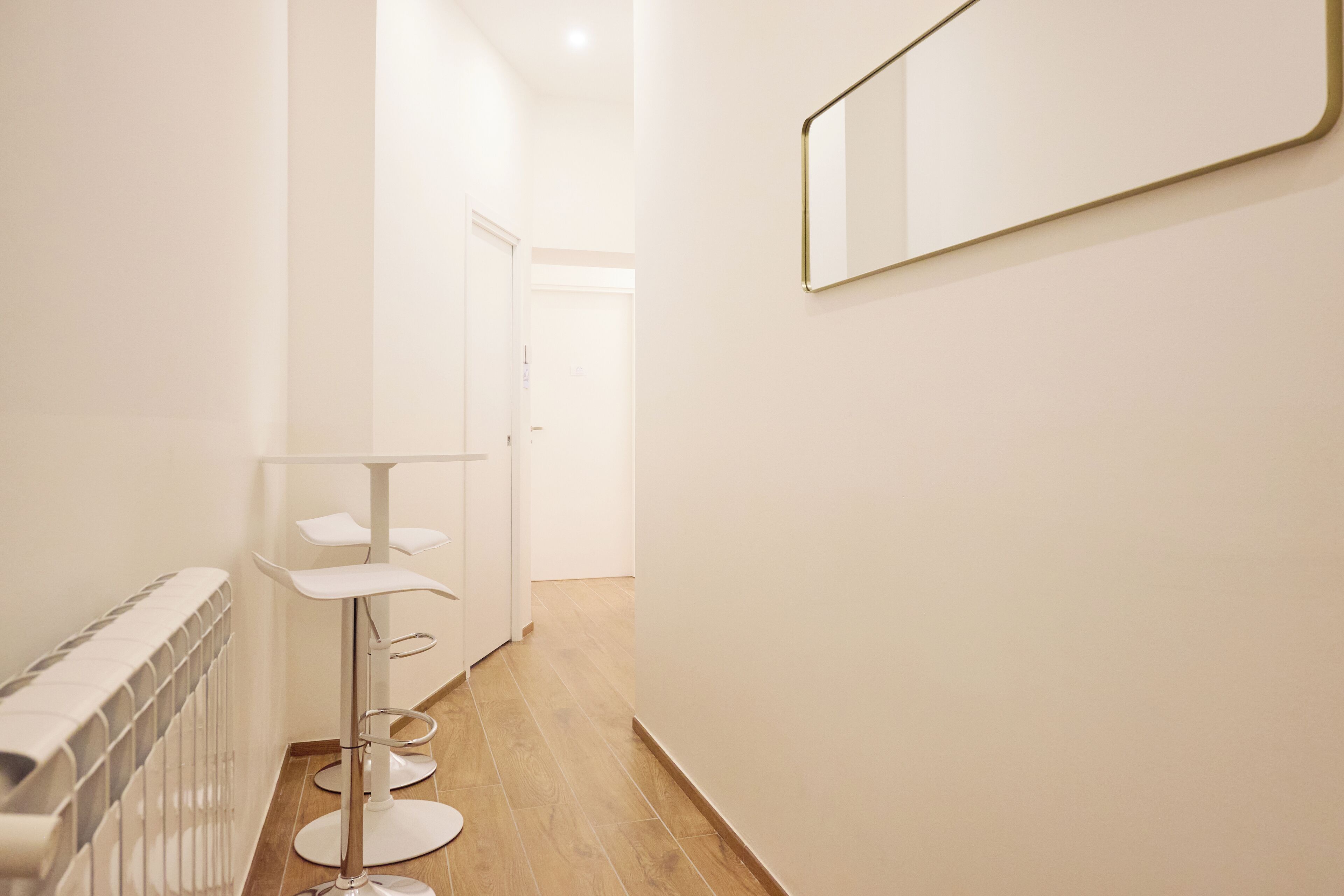 A narrow hallway with a radiator, a white floor, and a wall-mounted mirror.