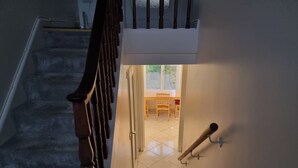 Una escalera con barandillas de madera que conduce a un cuarto con piso de baldosas y vistas a un espacio exterior con una mesa y sillas.