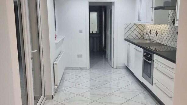 Una cocina estrecha con armarios blancos, suelo de baldosas y vistas a otra habitación.