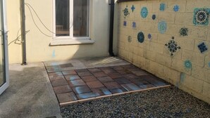 Un pequeño patio con suelo de baldosas, una ventana y un muro decorado con azulejos azules y verdes.