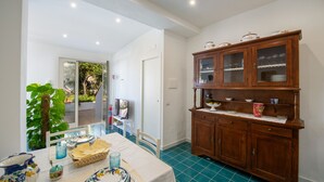 Un coin repas avec une table dressée pour deux personnes, un buffet en bois doté de portes en verre et une vue sur un jardin, accessible par une porte coulissante.