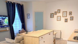 Un espace de vie compact comprenant un coin cuisine, un canapé, une table à manger et un téléviseur fixé au mur.