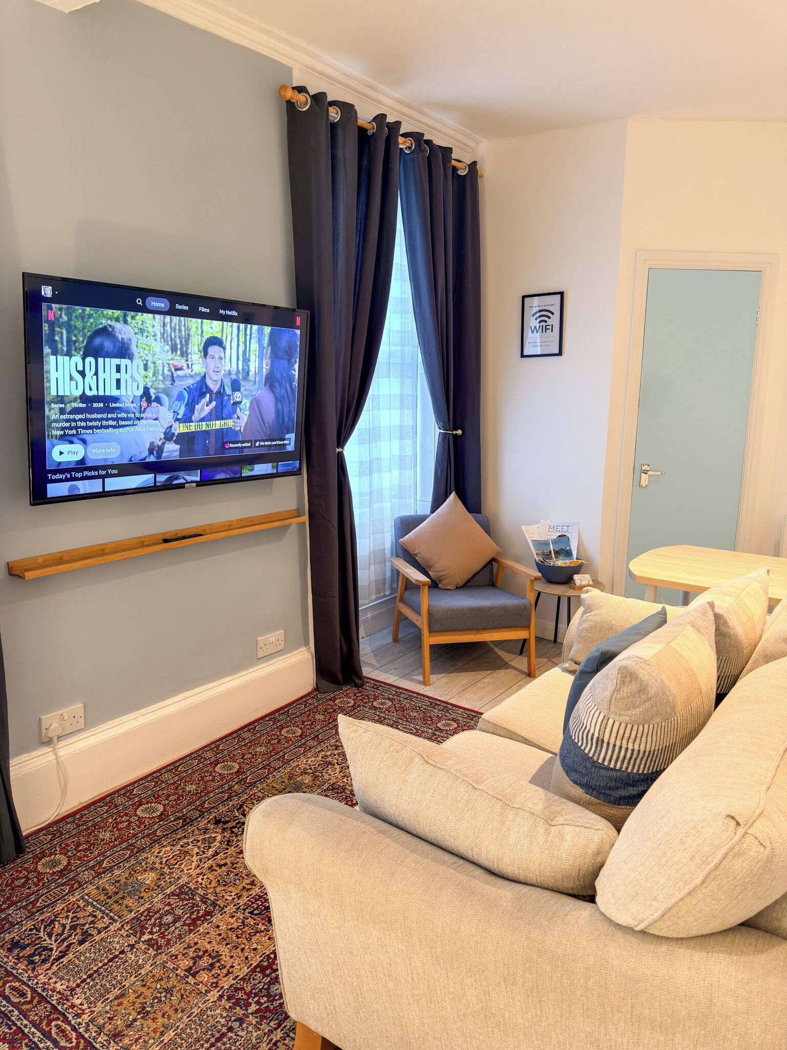 Un salon comprenant un téléviseur à écran plat, un canapé, un fauteuil, une petite table et une porte.