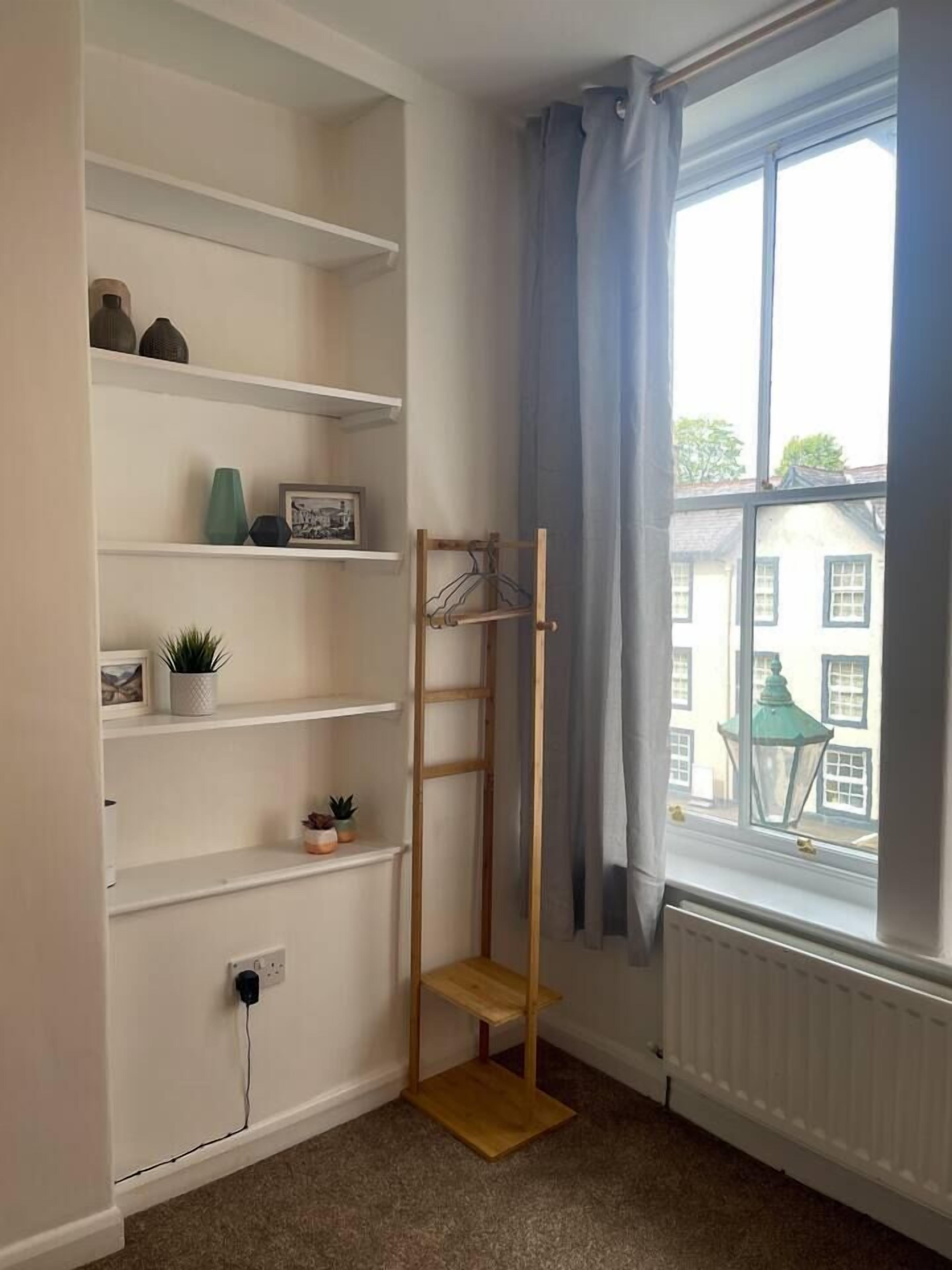 Et hjørneværelse med hvide reoler, en træstige, en radiator og et vindue med gardiner.