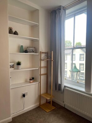 A corner room with a white shelving unit, a wooden ladder, a radiator, and a window with curtains. - The Studio, 2 bed flat, sleeps 4, Hadrian’s Wall, Brampton

 (Brampton)