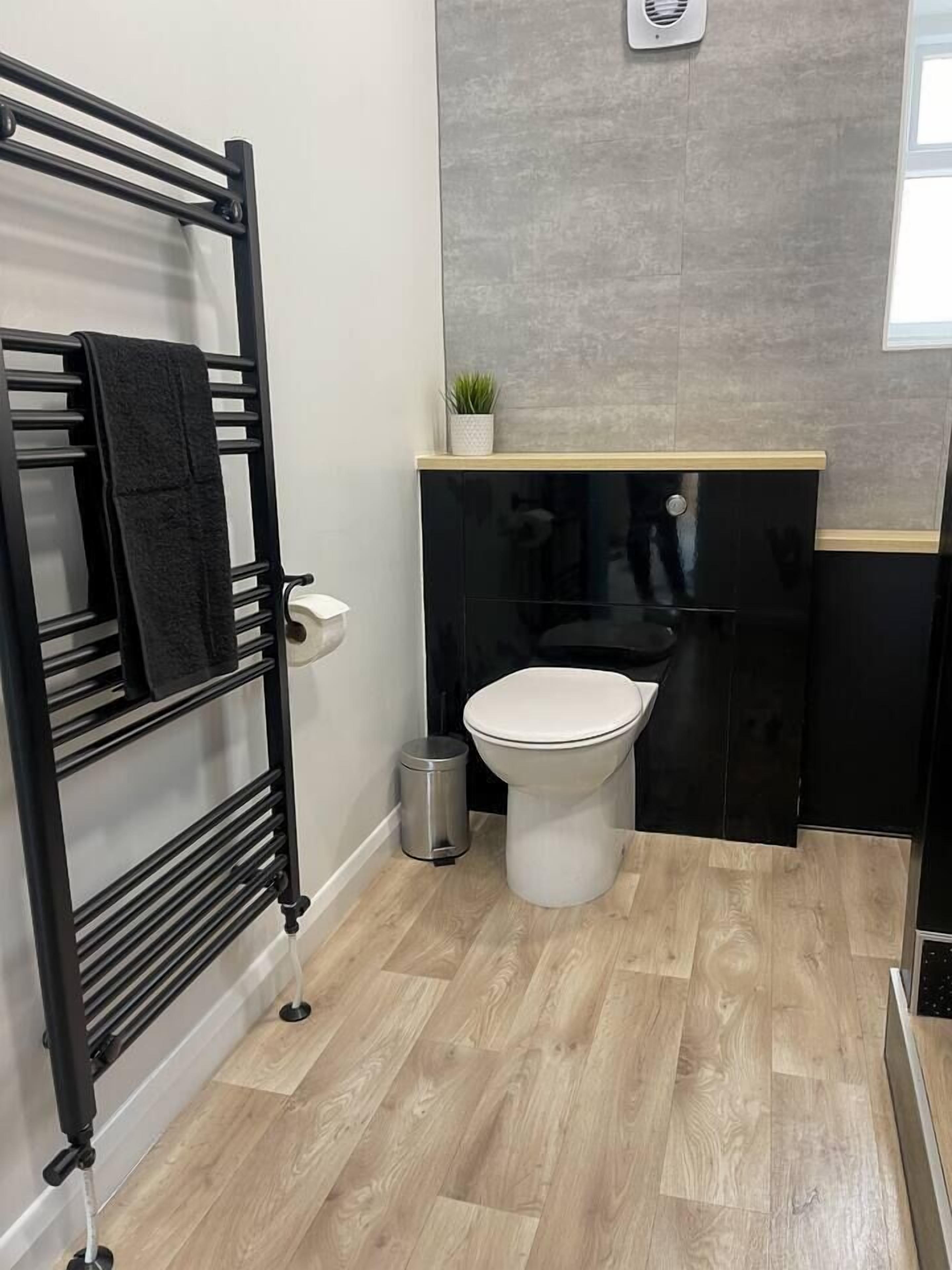 A bathroom with a black towel rack, a toilet, a trash bin, and a small potted plant on a shelf.