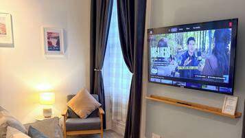 A hotel room with a television displaying a movie, a sofa, a chair, a lamp, and a rug.