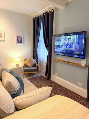 Habitación de hotel con una televisión mostrando una película, un sofá, una silla, una lámpara y una alfombra.