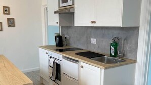 Une cuisine compacte avec des meubles blancs, un four à micro-ondes, un évier et une poubelle.