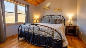 A bedroom with a metal bed frame, two bedside lamps, a window with curtains, and artwork on the walls. - Charming riverside with stunning views, cozy interiors, full amenities, and spacious decks. (Draper)