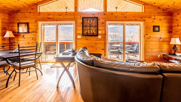 A cozy cabin interior with a wooden interior, a dining area, a seating area, and large windows. - Charming riverside with stunning views, cozy interiors, full amenities, and spacious decks. (Draper)