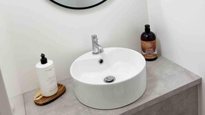 A bathroom with a round mirror, a white sink, and two bottles of liquid soap. - Cosy Annex sleeps 2 near Gretna, M6 Jct 45 / A75

 (Rigg)