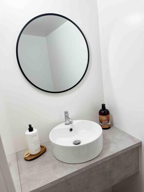 A bathroom with a round mirror, a white sink, and two bottles of liquid soap. - Cosy Annex sleeps 2 near Gretna, M6 Jct 45 / A75

 (Rigg)