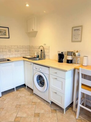 Une cuisine compacte équipée d’un lave-linge, d’un évier et d’une machine à café.