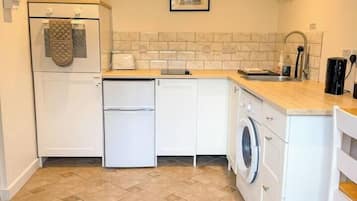 Une cuisine compacte avec des meubles blancs, un four à micro-ondes, un lave-linge et un dosseret carrelé.