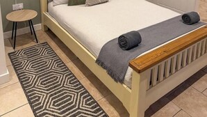 A neatly made bed with a wooden headboard, a bedside lamp, and a patterned rug. - Cosy Annex sleeps 2 near Gretna, M6 Jct 45 / A75

 (Rigg)