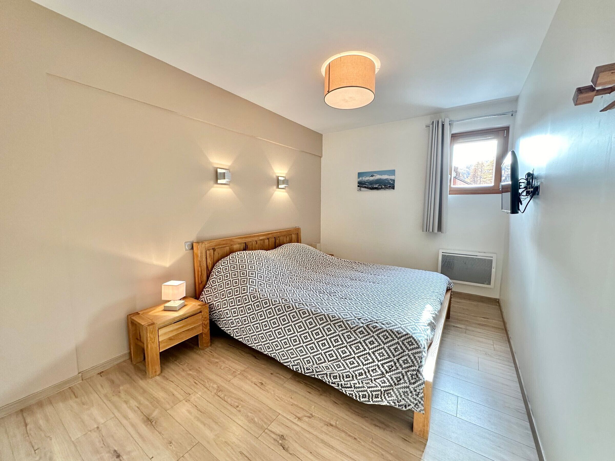 Ein Schlafzimmer mit einem hölzernen Bett, einem Nachttisch mit Lampe und einem Fenster mit Vorhängen.