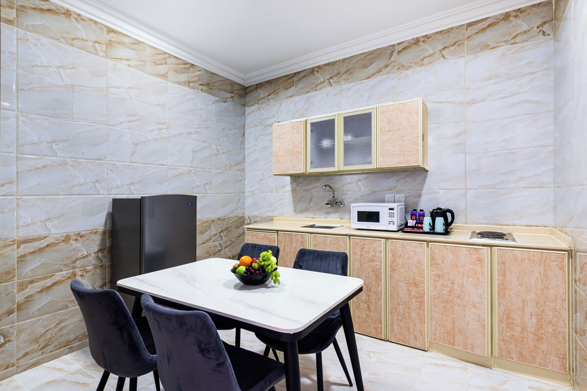 Una cocina moderna con paredes de mármol, una mesa de comedor con sillas, un refrigerador, un microondas y una cafetera.