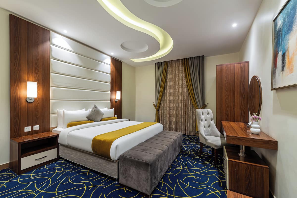 Habitación de hotel con una cama grande, un escritorio, una silla, una mesita de noche y un televisor montado en la pared.