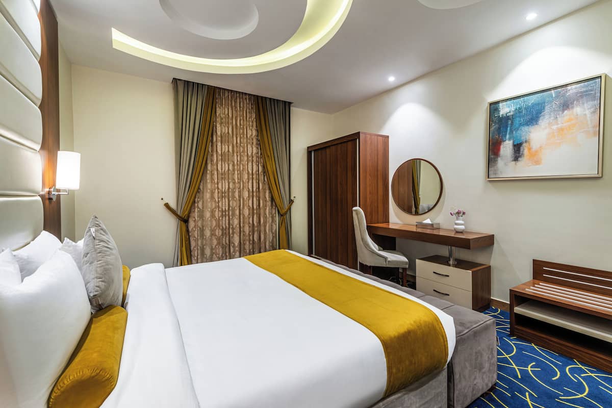 Habitación de hotel con cama, escritorio, silla, armario, espejo y un cuadro en la pared.