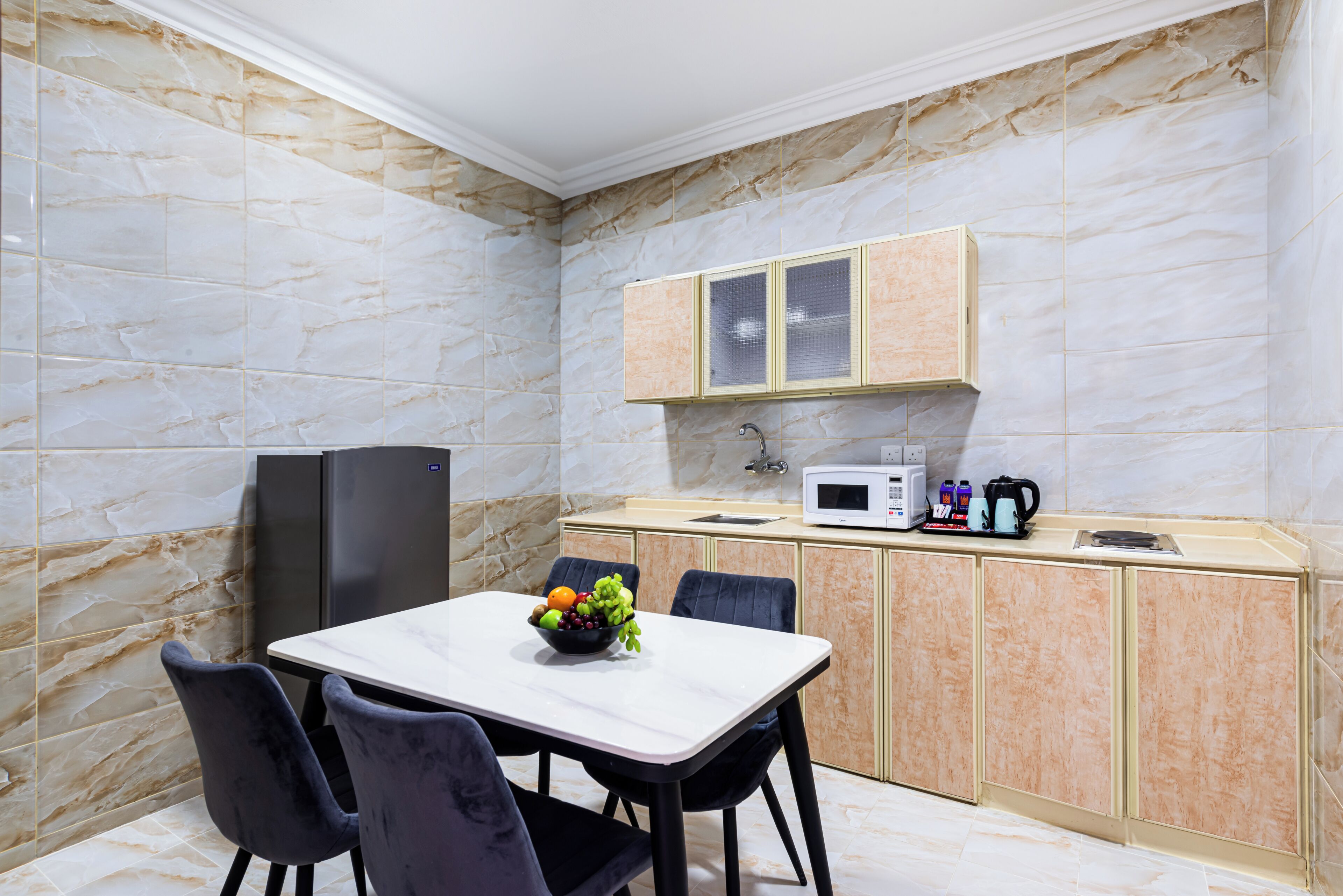 A modern kitchen with marble walls, a dining table with chairs, a refrigerator, a microwave, and a coffee maker.