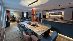 A modern living room with a wooden dining table, colorful chairs, a Christmas tree, and a kitchen area with a built-in island. - Workshop chalet ZH10 (Olsberg)