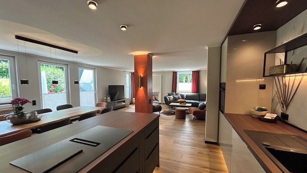 A modern kitchen with a central island, a dining area with a long table, and a living space with a sofa and a TV. - Workshop chalet ZH10 (Olsberg)