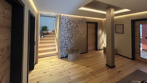 A modern interior with a wooden floor, a staircase, and a decorative wall with leaf patterns. - Workshop chalet ZH10 (Olsberg)