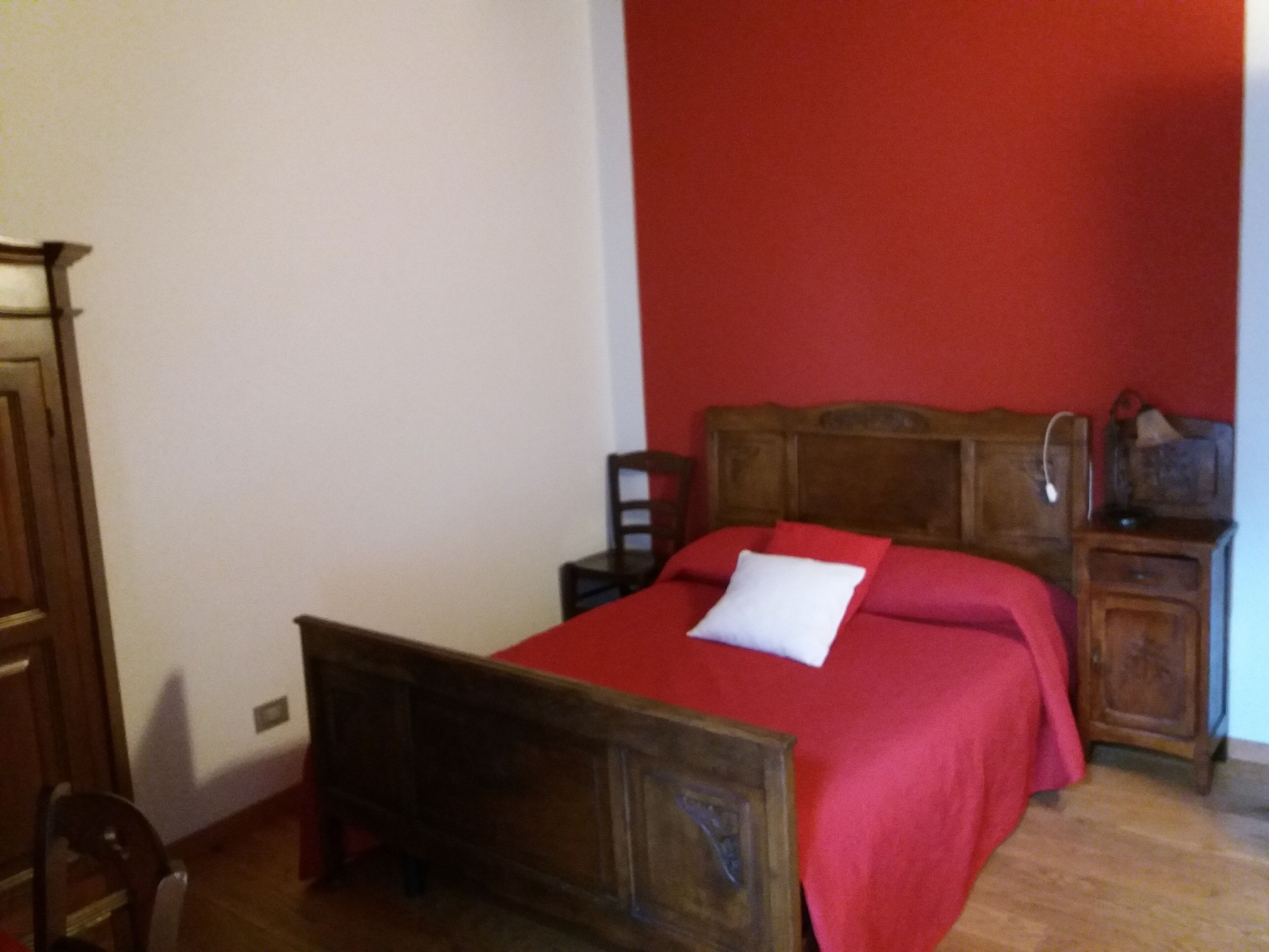 Un dormitorio con una cama de madera, una pared roja y una mesita de noche de madera con una lámpara.