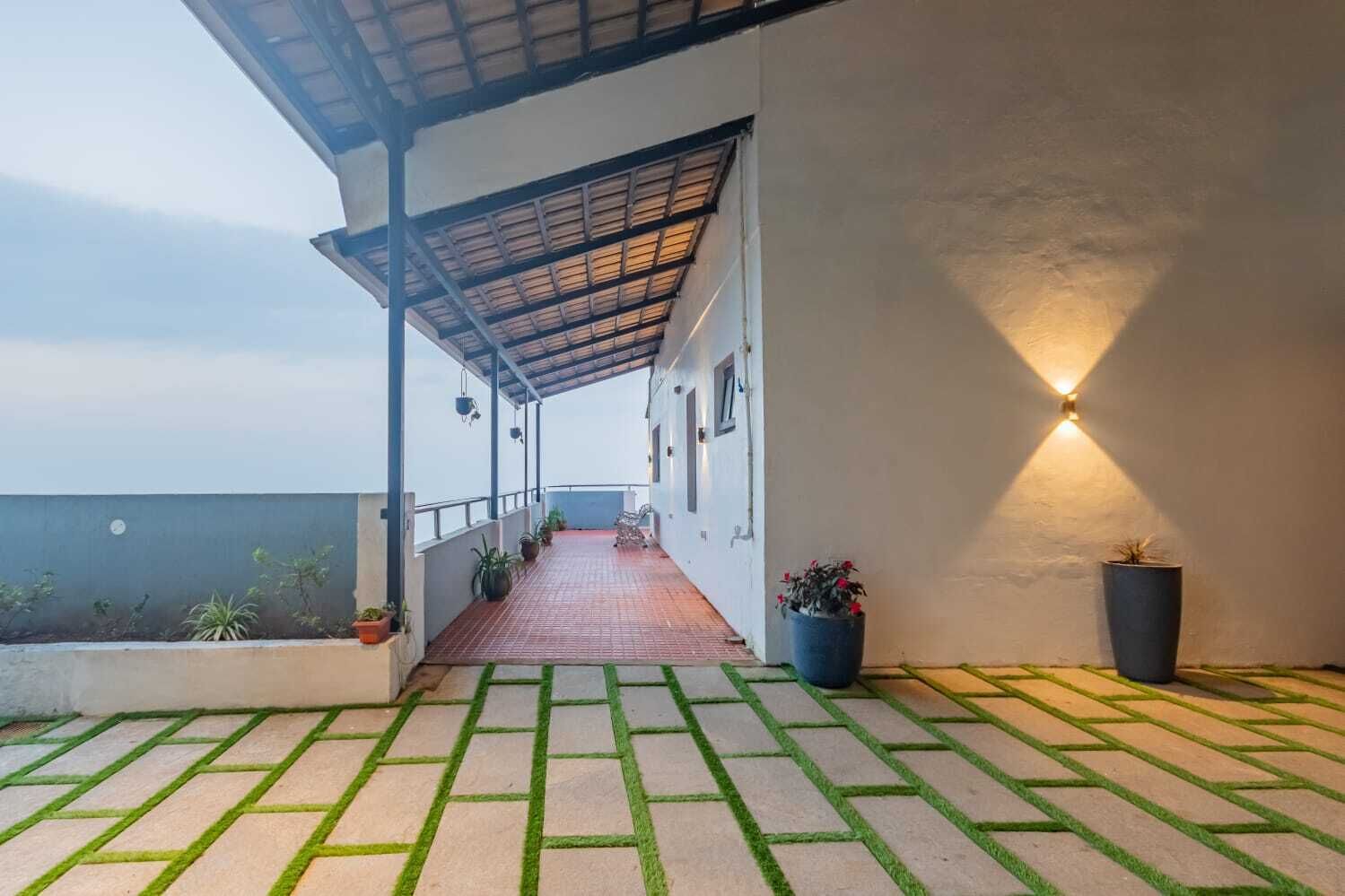 A covered walkway with potted plants, a tiled floor, and a wall-mounted light fixture.