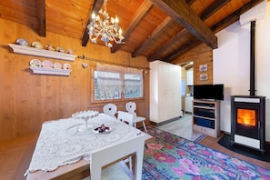 A wooden interior with a dining table, chairs, a chandelier, a fireplace, and a television.