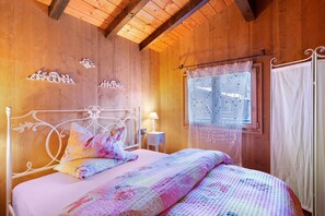 A wooden room with a bed, a window with lace curtains, and decorative wall elements.