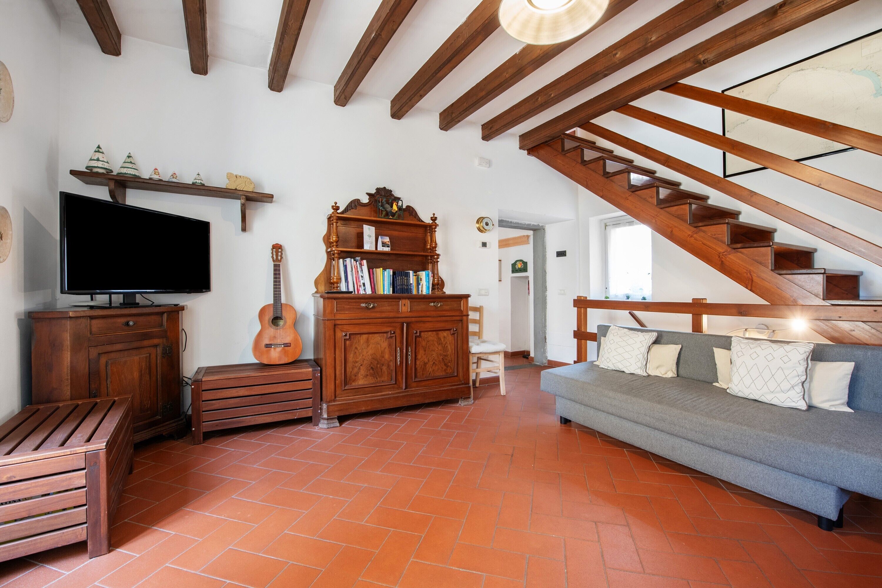 A living room with a TV, wooden furniture, a guitar, a bookshelf, a sofa, and a staircase.