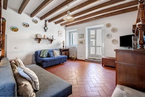 Una stanza con soffitto in legno, un divano blu, un armadio in legno e un televisore.